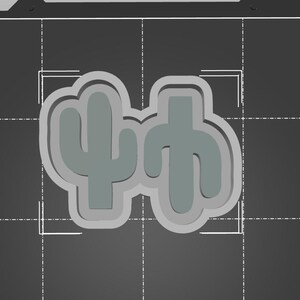 May include: Two green cactus cookie cutters, one with a single arm and the other with two arms, on a gray background.
