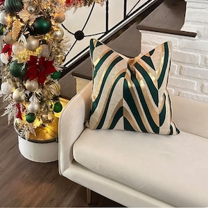 May include: A white couch with a green and gold patterned throw pillow. The couch is in front of a white brick wall and a staircase.
