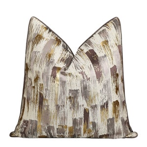 May include: Decorative throw pillow with a brushstroke design in shades of cream, gold, gray, and brown. The pillow has a textured appearance and a dark brown border. This accent pillow adds a touch of elegance to any living space.