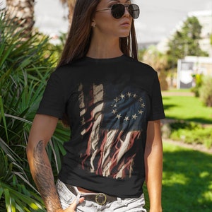 May include: A black t-shirt with a distressed American flag design featuring 13 stars in a circle. The flag is faded and has a vintage look.