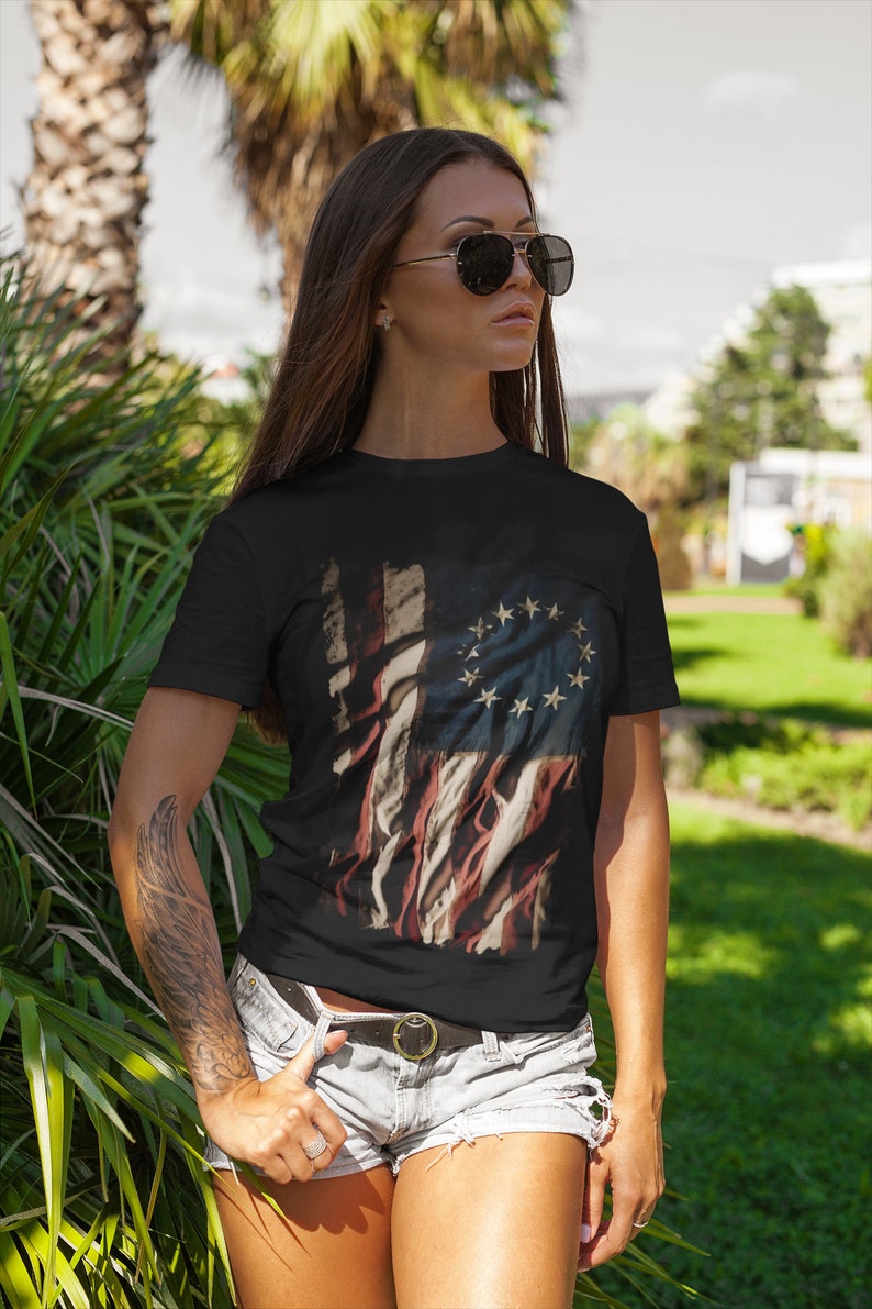 May include: A black t-shirt with a distressed American flag design featuring 13 stars in a circle. The flag is faded and has a vintage look.