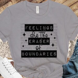 Può includere: Maglietta grigia con testo nero che recita "Feelings are the eraser of boundaries". Il testo è circondato da piccole stelle bianche.