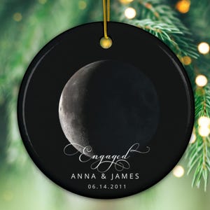 Puede incluir: Adorno de cerámica negro y blanco con una luna creciente y el texto "Engaged Anna & James 06.14.2011".