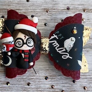 May include: A red and gold Christmas hair bow with a Harry Potter character wearing a Santa hat and holding a small owl. The bow has a black background with the text "Happy Xmas" and a white owl.