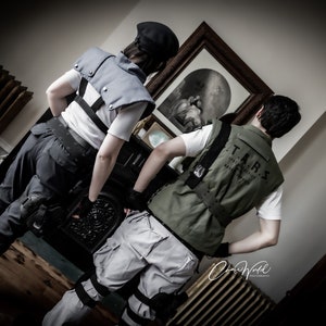 May include: Two people dressed in tactical gear, one wearing a black vest and the other a green vest with the text "T.A.R.S. Special Tactics and Rescue Service" printed on the back.
