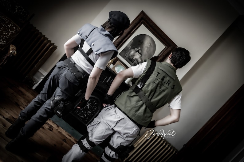 May include: Two people dressed in tactical gear, one wearing a black vest and the other a green vest with the text "T.A.R.S. Special Tactics and Rescue Service" printed on the back.