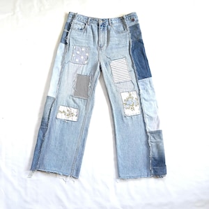 Pode incluir: Jeans de ganga de lavagem clara com detalhes de patchwork. Os patches incluem bolinhas brancas, listras azuis e brancas, bordados florais e ganga lisa. Os jeans têm pernas largas e bainha crua.