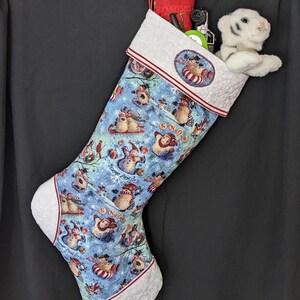 Könnte beinhalten: Ein blauer und weißer Weihnachtsstrumpf mit einem Schneemannmuster. Der Strumpf ist gefüllt mit einem Stofftier, einem roten Kissen und anderen kleinen Geschenken. Der Strumpf hat einen grauen Bund mit einem roten und weißen Besatz.