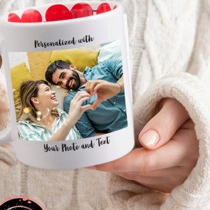 Puede incluir: Taza de cerámica blanca con una foto de una pareja haciendo un corazón con las manos. La taza tiene el texto "Personalizado con" y "Tu foto y texto". La parte superior de la taza está llena de caramelos rojos en forma de corazón.