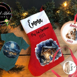 May include: A set of personalized Christmas gifts featuring a red stocking with a nativity scene, a green baby onesie with a moonlit scene, a round wooden ornament with a nativity scene and the name "Annie", and a round tag with the text "To Becky".