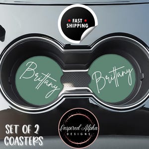May include: Set of two car coasters with the name "Brittany" in white script on a green background. The coasters are in a car cup holder. The image also includes a "Fast Shipping" sticker and a logo.