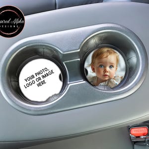 May include: Two gray car cup holders with a white round coaster in each. The coaster on the left says "YOUR PHOTO, LOGO OR IMAGE HERE". The coaster on the right has a photo of a baby girl with blonde hair and blue eyes.