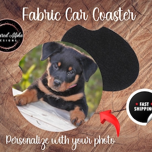 May include: A black and tan puppy with a pink collar is looking at the camera. The puppy is on a white wooden surface. The image is in a circle shape and is surrounded by a wooden background. The text "Fabric Car Coaster" is at the top of the image. The text "Personalize with your photo" is at the bottom of the image.