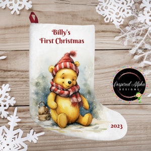 May include: A white Christmas stocking featuring a Winnie the Pooh illustration wearing a red and white striped hat and a red scarf. The stocking is printed with the text "Billy's First Christmas" and "2023".
