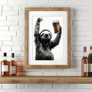 Könnte beinhalten: Ein Schwarzweißfoto eines Faultiers, das ein Glas Bier hält. Das Foto ist in einem Holzrahmen gerahmt und hängt an einer weißen Backsteinwand. Unter dem Foto befinden sich zwei Flaschen Schnaps auf einem Holzregal.