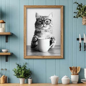 May include: A black and white photo of a cat wearing glasses and holding a white mug. The cat is sitting on a wooden table. The photo is framed in a brown wooden frame.