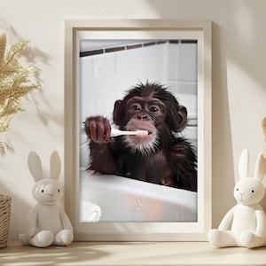May include: A framed print showing a chimpanzee brushing its teeth in a bathtub. The chimpanzee has dark brown fur and is holding a white toothbrush. The bathroom is white, and the print is in a light-coloured frame.