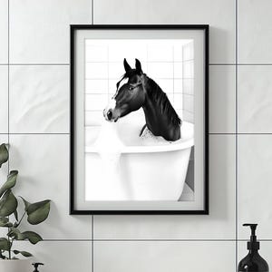 May include: A black and white photograph of a horse in a bathtub. The horse is looking to the left and has its head and neck in the water. The bathtub is white and has a black rim.