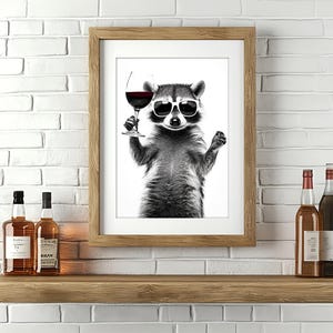 May include: A black and white illustration of a raccoon wearing sunglasses and holding a glass of red wine. The raccoon is in front of a wooden frame with a white background. Two bottles of liquor are on a wooden shelf below the frame.