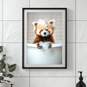 May include: Framed print of a red panda enjoying a bubble bath in a white tub. The red panda has reddish-brown and white fur. The print is mounted on a white tiled wall. The image is framed in black.