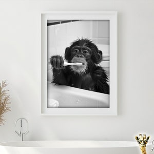 May include: A black and white photograph of a chimpanzee brushing its teeth in a bathtub. The chimpanzee is looking directly at the camera and has a toothbrush in its mouth. The photo is framed in a white frame.