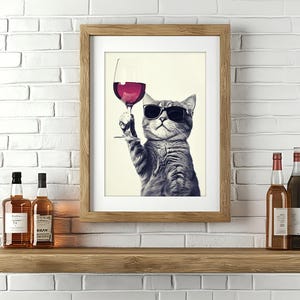 Puede incluir: Una impresión enmarcada de un gato con gafas de sol y sosteniendo una copa de vino tinto. El gato está mirando a la cámara. La impresión está en un estante de madera con dos botellas de licor.