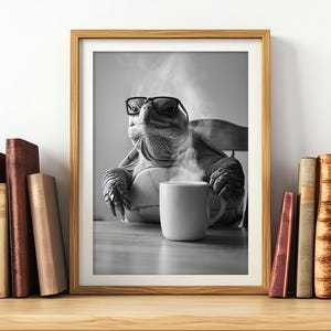 Può includere: Una foto in bianco e nero di una tartaruga che indossa gli occhiali e tiene una tazza di caffè fumante. La tartaruga è seduta a un tavolo con un libro sullo sfondo.