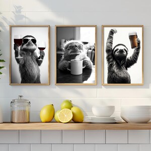 Könnte beinhalten: Set aus drei gerahmten Schwarz-Weiß-Drucken mit Faultieren. Ein Faultier trägt eine Sonnenbrille und hält Weingläser, ein anderes nippt an einer Tasse und das dritte hebt ein Bier. Die Drucke werden an einer weißen Wand ausgestellt.