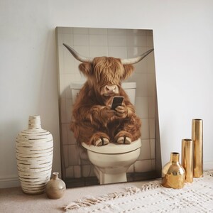 May include: A brown and white Highland cow sits on a white toilet, looking at a smartphone in its hooves. The cow is in a tiled bathroom with white walls.