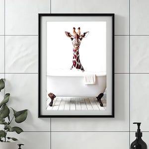 May include: A framed art print showing a giraffe in a bathtub. The giraffe's head and neck are visible, with a brown and white patterned coat. The white bathtub has claw feet, and a white towel is draped over the edge.
