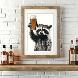 May include: A framed print of a raccoon holding a glass of beer. The raccoon is looking at the camera. The print is on a wooden shelf with two bottles of liquor.