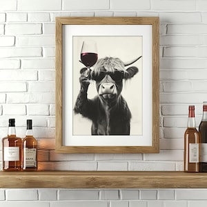 May include: A framed print of a Highland cow wearing sunglasses and holding a glass of red wine. The print is hanging on a white brick wall above a wooden shelf with two bottles of liquor.