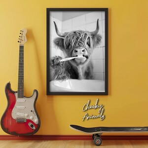 May include: Black and white photo of a Highland cow brushing its teeth with a toothbrush. The photo is framed and hanging on a yellow wall. The text "Cheeky Animals" is written below the frame.