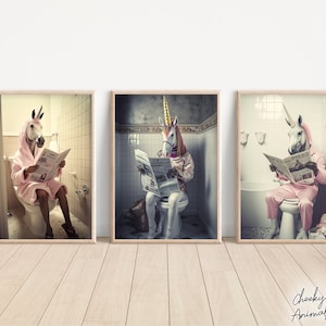May include: Three framed prints of a unicorn wearing a pink bathrobe and reading a newspaper while sitting on a toilet. The unicorn is in a bathroom setting with white tiled walls.