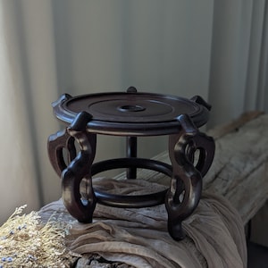 Puede incluir: Soporte de exhibici&oacute;n de madera marr&oacute;n oscuro con una parte superior redonda y patas curvas ornamentadas. El soporte tiene una base circular y una columna de soporte central. La madera tiene un acabado pulido y est&aacute; dise&ntilde;ado para un objeto decorativo.