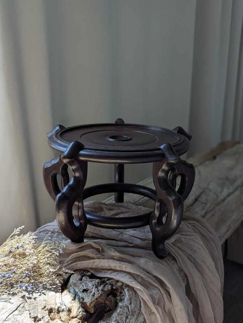Puede incluir: Soporte de exhibici&oacute;n de madera marr&oacute;n oscuro con una parte superior redonda y patas curvas ornamentadas. El soporte tiene una base circular y una columna de soporte central. La madera tiene un acabado pulido y est&aacute; dise&ntilde;ado para un objeto decorativo.