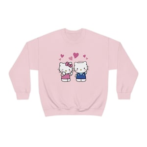 Può includere: Felpa rosa con una grafica di Hello Kitty e Dear Daniel che si tengono per mano con cuori rosa intorno a loro.