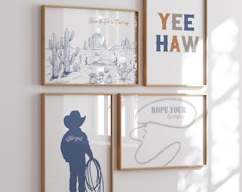 May include: Four framed prints with a western theme. The top left print features a desert landscape with cacti and the text "Born to Be a Cowboy". The top right print features the text "YEE HAW" in blue, orange, and gray. The bottom left print features a silhouette of a cowboy with the text "little gent". The bottom right print features a lasso with the text "Rope Your Dreams".