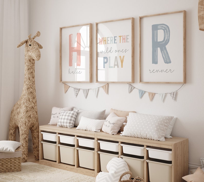 May include: A light wood storage bench with six white and beige storage bins. The bench is decorated with a string of pastel colored flags and three framed prints. The prints feature the letters H and R in pink and blue, and the text "WHERE THE wild ones PLAY".