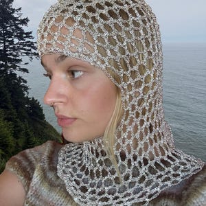May include: A metallic silver crochet hood featuring an open, diamond-shaped mesh pattern that covers the head and extends down to the neck and shoulders, crafted from a shimmering, reflective yarn material with a distinct, repeating chain-like texture.