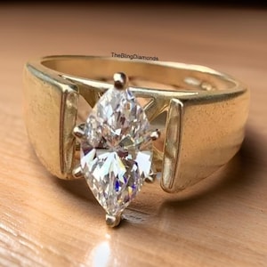 May include: A gold ring featuring a large marquise-shaped diamond set in a prong setting. The ring has a thick band with a decorative design.