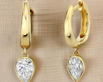 May include: A pair of gold hoop earrings with pear-shaped diamond pendants. The earrings have a polished finish and a secure clasp. The diamonds are clear and sparkling, set in a gold bezel. The earrings are displayed on a neutral background.