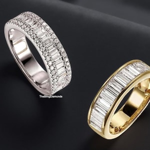 Puede incluir: Dos anillos de diamantes sobre una superficie negra. Un anillo es plateado con una fila de diamantes pequeños y una fila de diamantes baguette. El otro anillo es dorado con diamantes baguette.