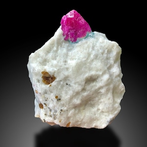 May include: A bright pink ruby crystal on a white matrix with brown crystals.