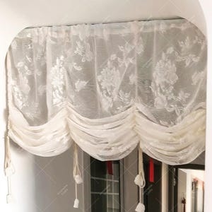 May include: White sheer curtain with a floral pattern and a gathered design. The curtain is hung from a ceiling and has tassels on the ends.