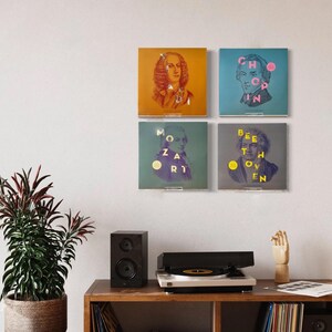 May include: Four framed prints of famous composers, including Mozart, Beethoven, Chopin, and Bach. The prints are displayed on a white wall above a record player and a wooden shelf with records.
