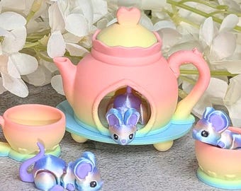 May include: A miniature pastel rainbow teapot set featuring a gradient of pink, yellow, and blue. The set includes a teapot with a heart-shaped lid knob, two matching cups, and three small mouse figurines in shades of blue and purple.