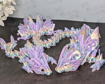 May include: Two articulated dragon figures in shades of lavender, blue, and gold. The dragons are 3D printed with intricate details, including crystal-like structures along their bodies. The text "PLAYFUL PRINTS" is visible in the background.