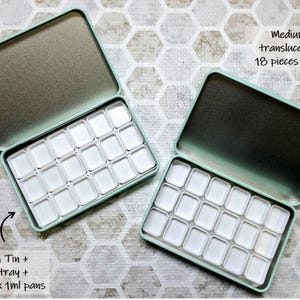 May include: Two mint green metal tins, each containing a tray with 18 empty 1ml pans. One tin features a white tray, while the other includes a translucent tray. Text on the image reads: Medium Tin + White tray + 18 pieces x 1ml pans and Medium Tin + translucent tray + 18 pieces x 1ml pans.