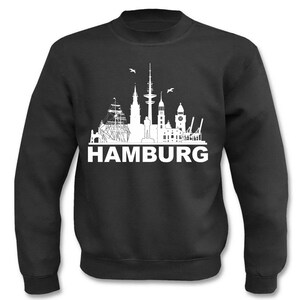 Op de afbeelding: Zwart sweatshirt met een wit silhouet van de skyline van Hamburg en het woord "HAMBURG" eronder gedrukt.